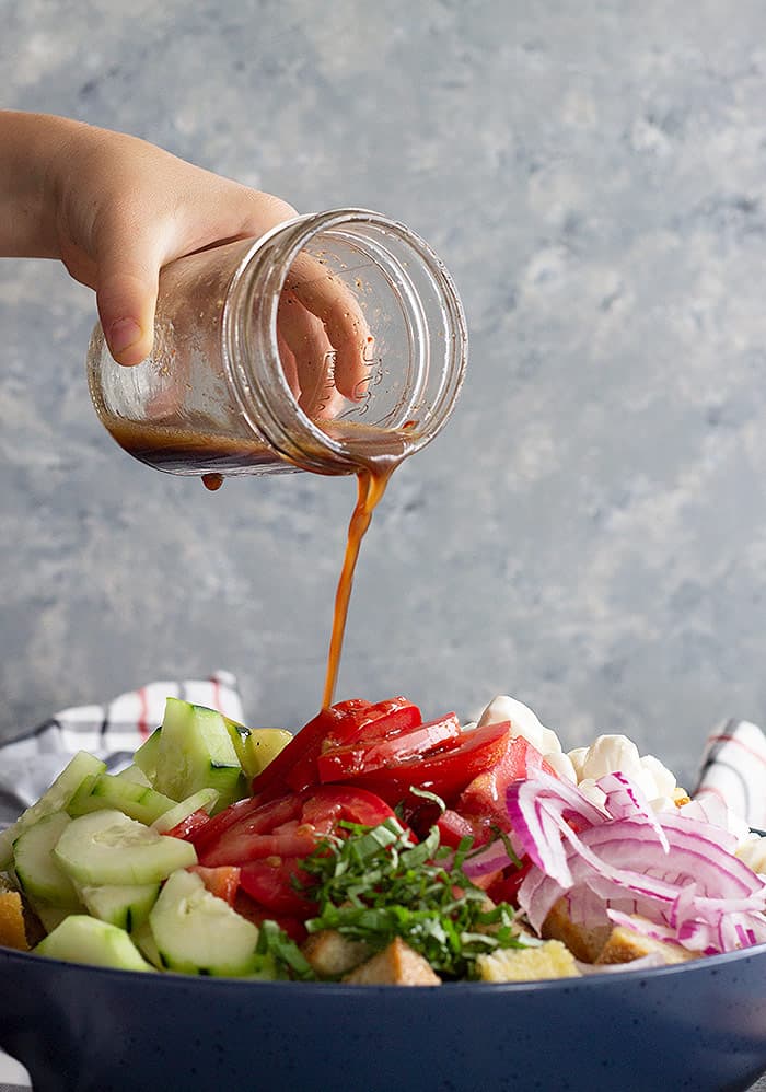 Dressing pouring over panzanella salad.