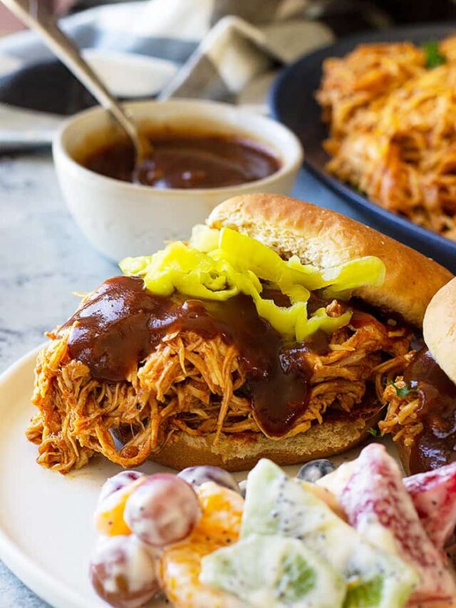 Close up picture of slow cooker bbq chicken on a bun with bbq sauce.