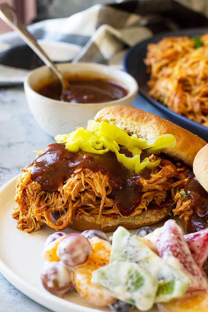 Close up picture of slow cooker bbq chicken on a bun with bbq sauce.