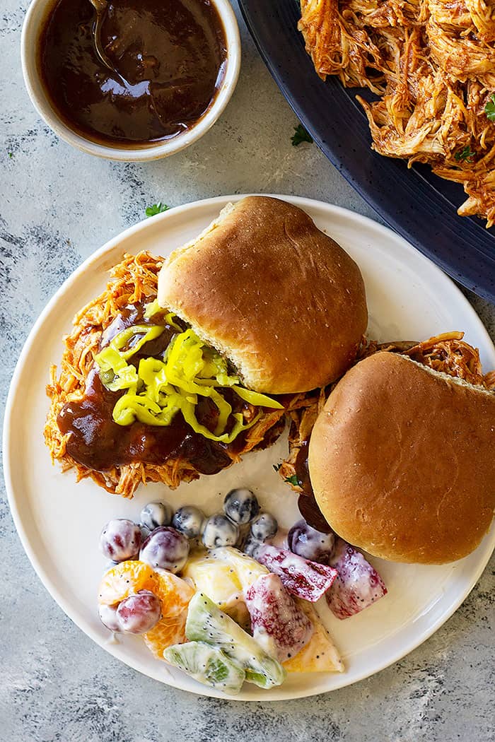 Plate of slow cooker bbq chicken sandwiches with bbq sauce. 