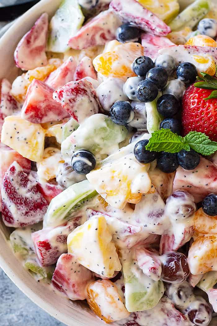 Close up of creamy fruit salad in a bowl garnished with fresh blueberries and mint. 