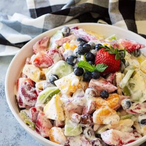 Creamy Fruit Salad mixed and in a large bowl. Garnished with fresh blueberries and mint.