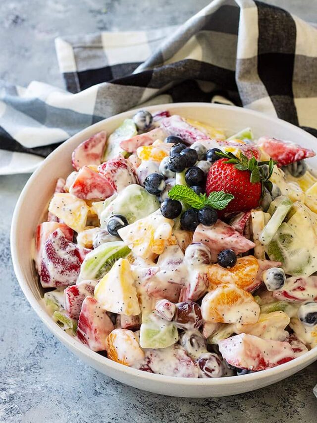 Creamy Fruit Salad mixed and in a large bowl. Garnished with fresh blueberries and mint.
