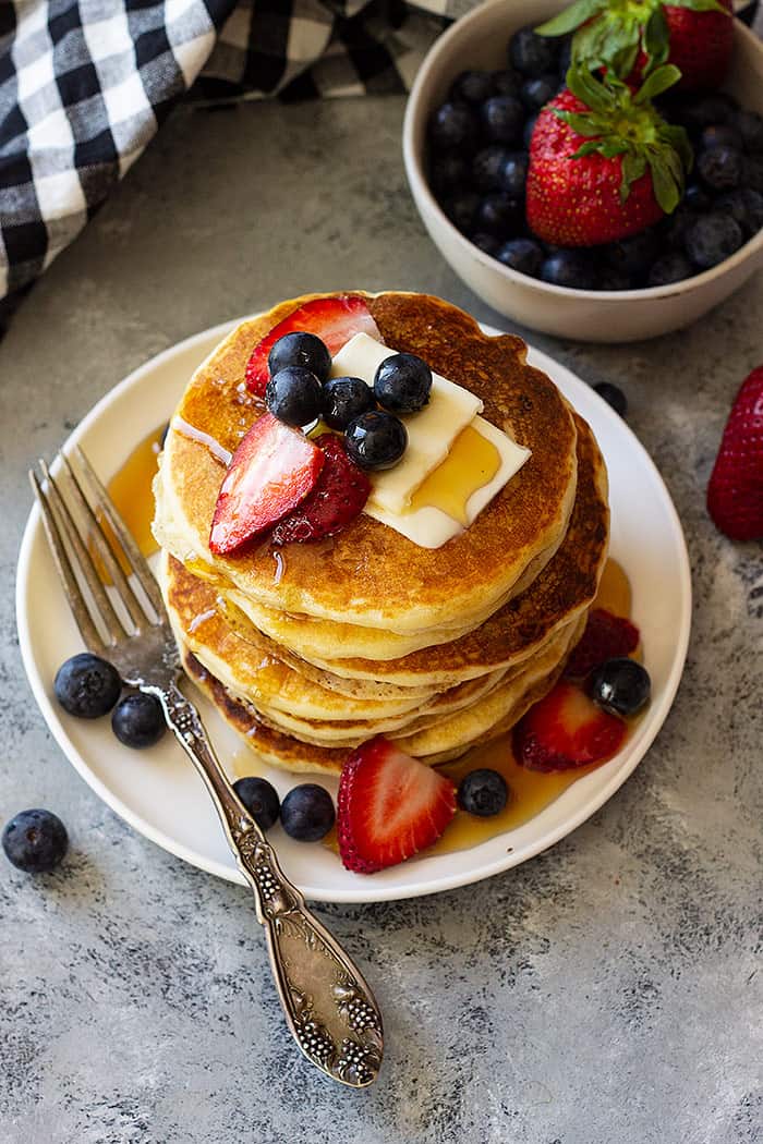 Looking down on a stack of fluffy buttermilk pancakes smothered in syrup, pats of butter, and berries.