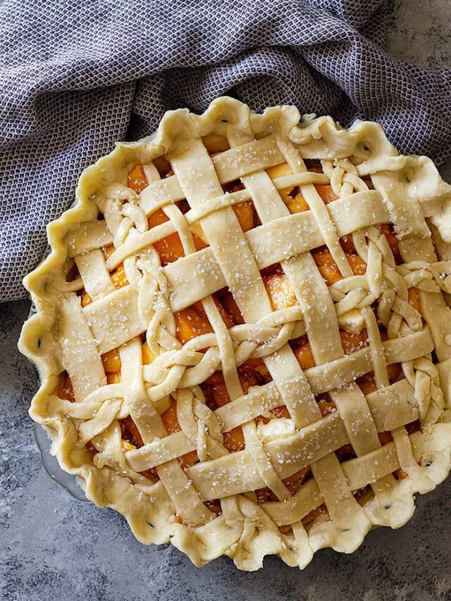 Top down view of a peach pie with an all butter crust lattice top.