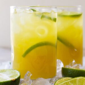 Tall glass of classic margarita with lime wedges and ice.