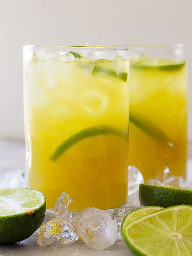 Tall glass of classic margarita with lime wedges and ice.