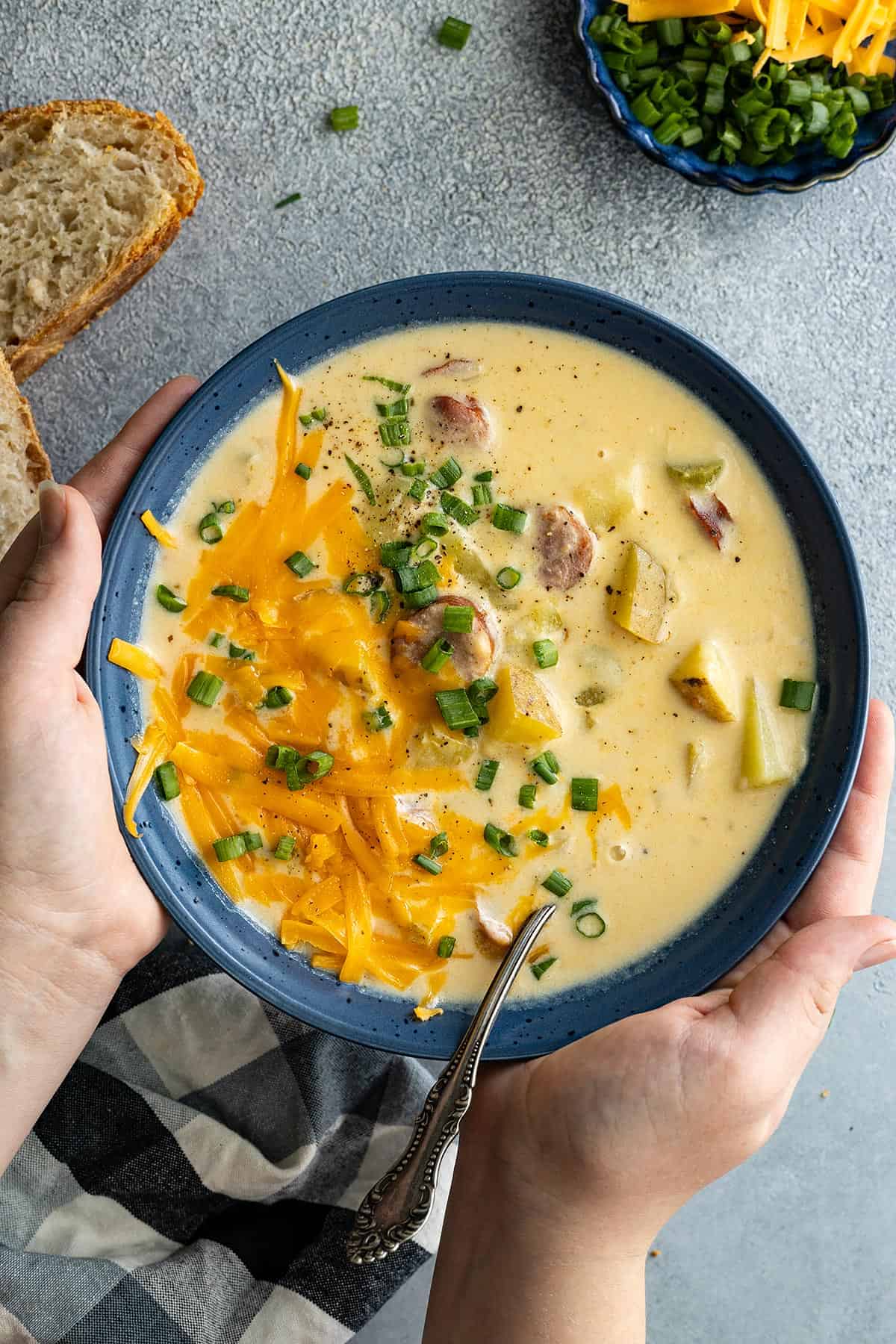 Hands holding a bowl of cajun potato soup garnished with cheese and green onion.