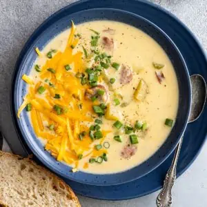 Overhead view of creamy cajun potato soup in a blue bowl. Garnished with cheese and green onion and a piece of crusty bread off to the side.