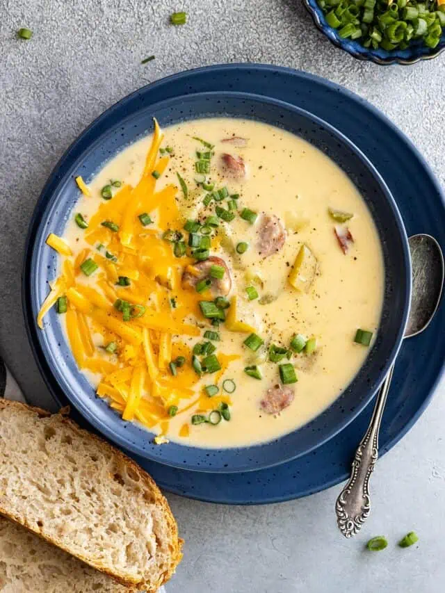 Overhead view of creamy cajun potato soup in a blue bowl. Garnished with cheese and green onion and a piece of crusty bread off to the side.