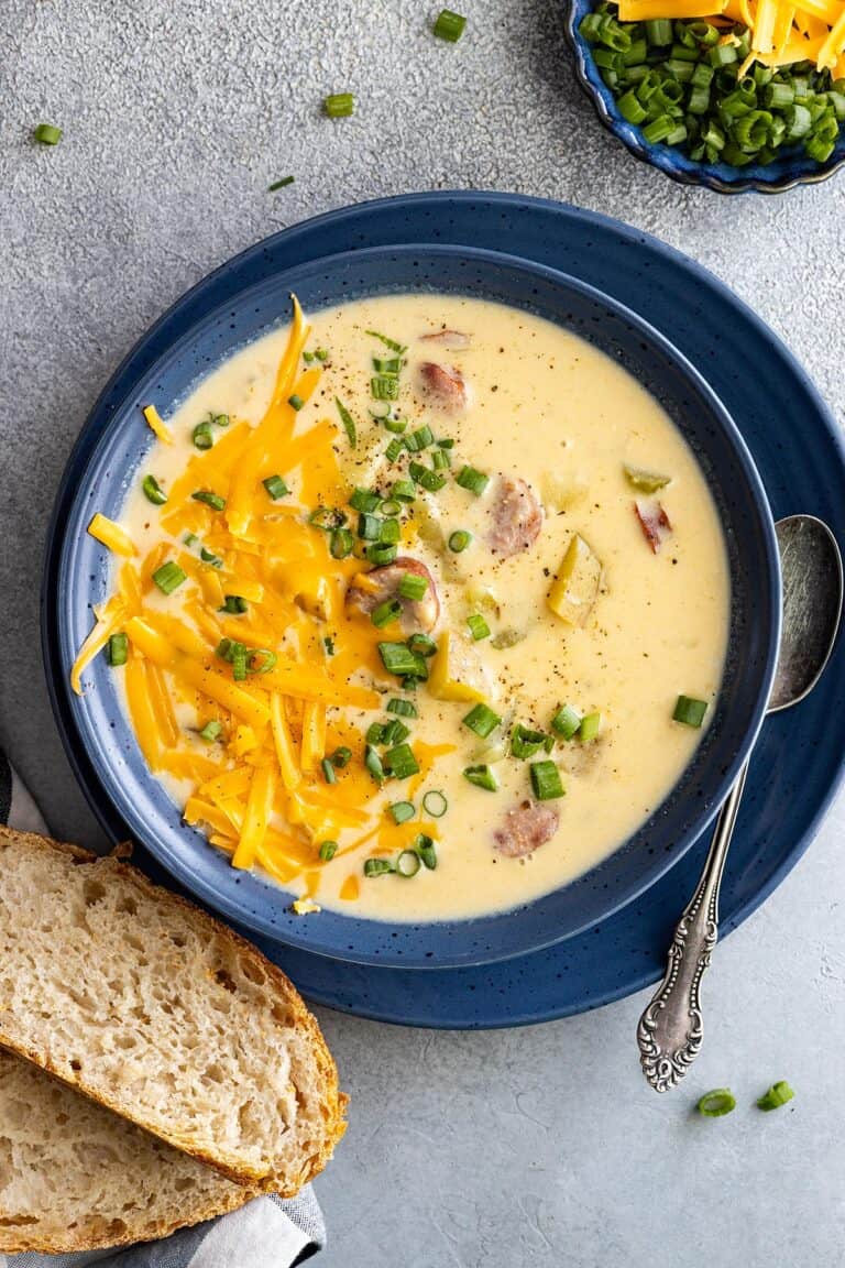 Overhead view of creamy cajun potato soup in a blue bowl. Garnished with cheese and green onion and a piece of crusty bread off to the side.