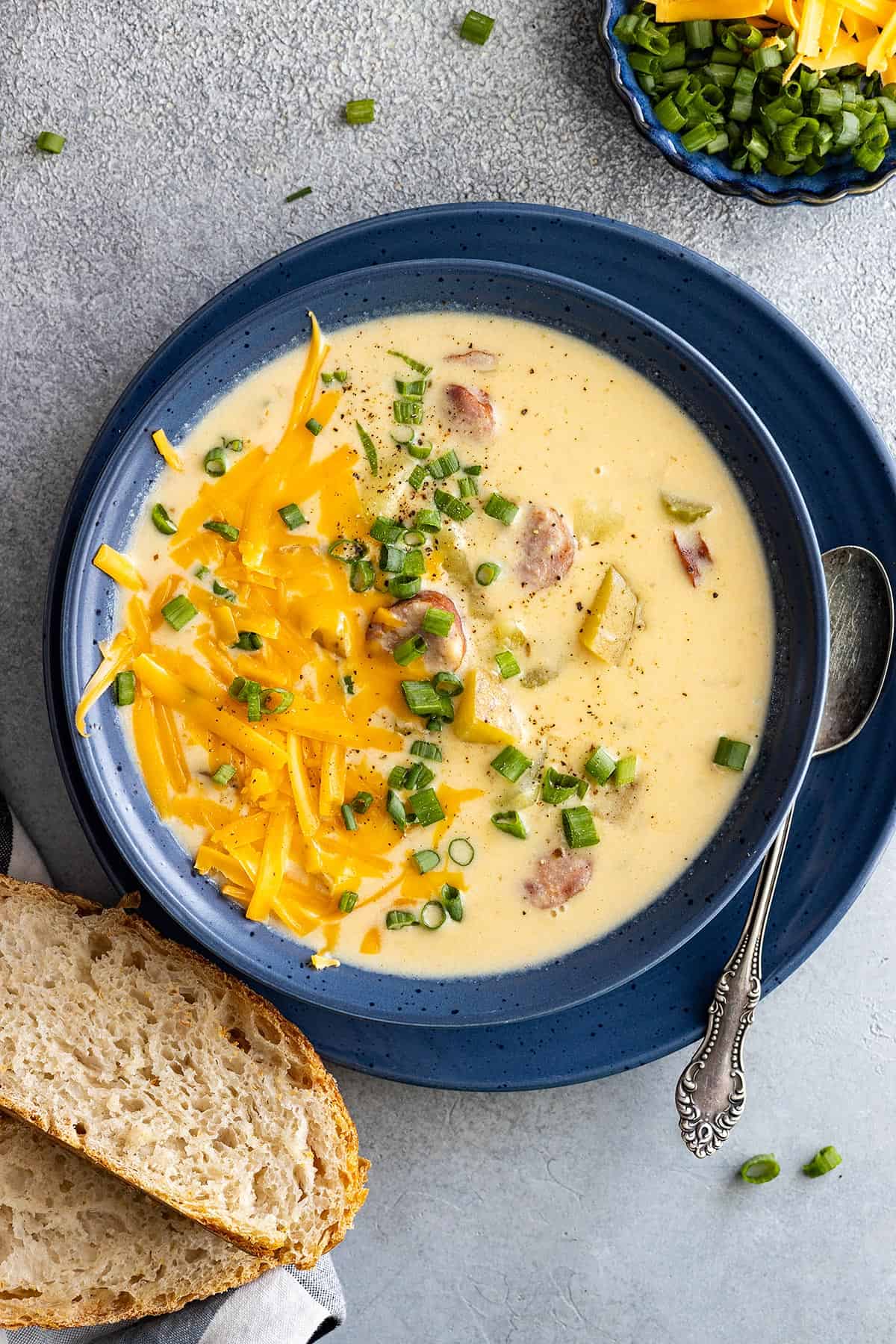 Overhead view of creamy cajun potato soup in a blue bowl. Garnished with cheese and green onion and a piece of crusty bread off to the side. 