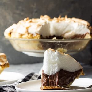 Slice of chocolate meringue pie on a plate with a bite taken out.