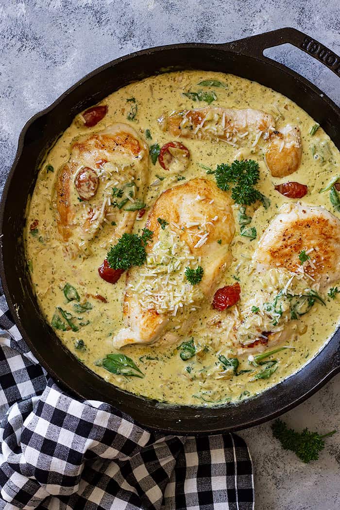 Skillet with creamy tuscan chicken garnished with fresh parsley.
