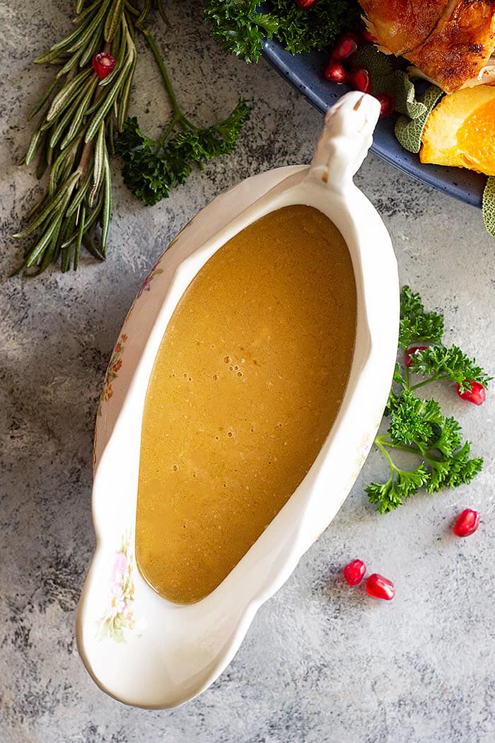 Homemade turkey gravy in a gravy boat. Fresh herbs and pomegranate seeds scattered around as decoration.