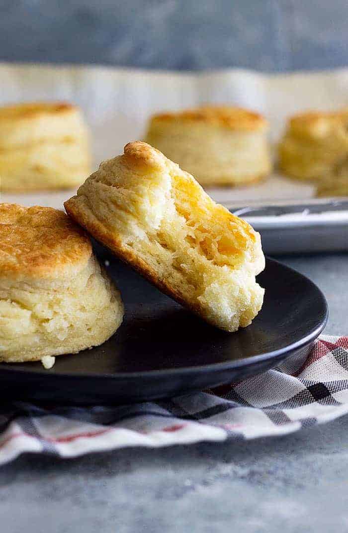 Flaky buttermilk biscuit with bite on black plate. 