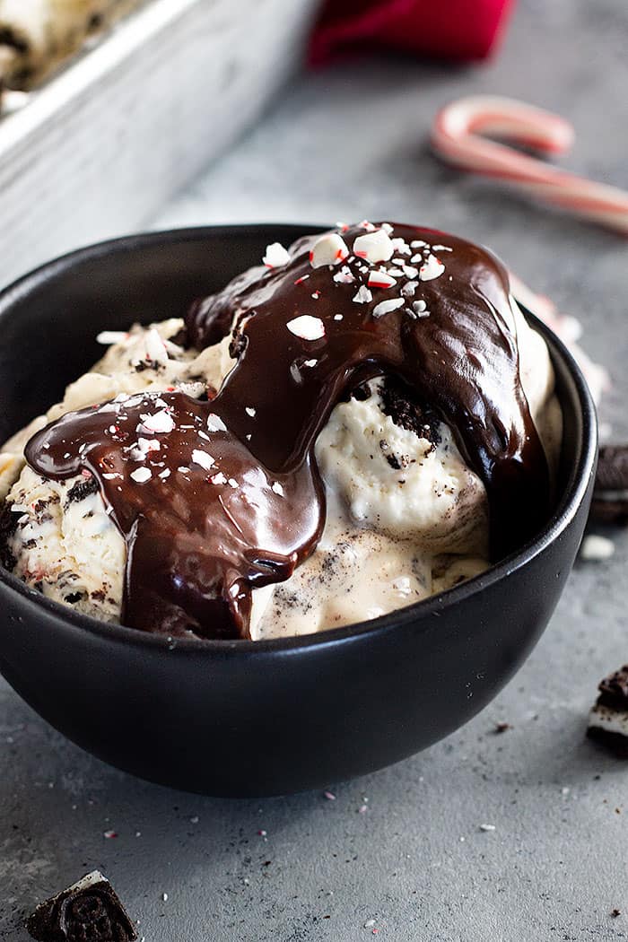 A bowl of no churn peppermint cookie ice cream topped with homemade hot fudge sauce, chopped oreos, and crushed peppermints.