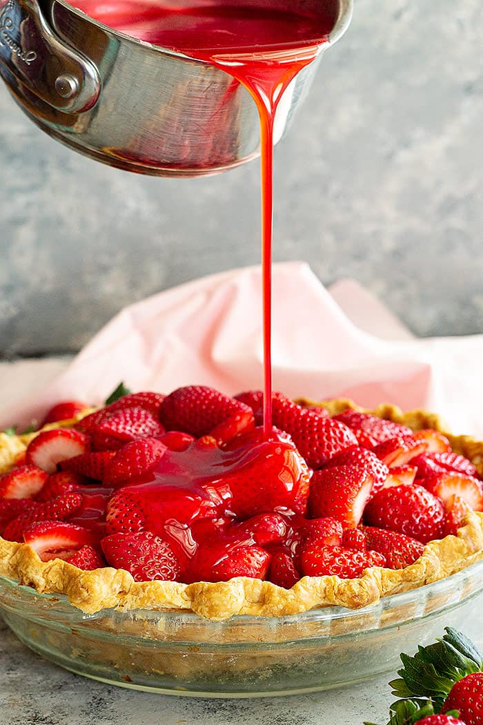 Pouring strawberry jello filling over the pie. 