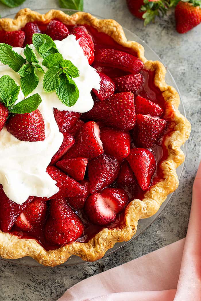 Top down view of strawberry pie topped with freshly whipped cream and mint.