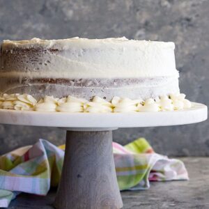 A cake on a stand covered in cream cheese frosting.