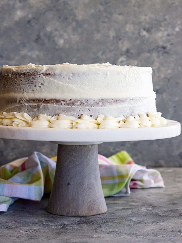 A cake on a stand covered in cream cheese frosting.