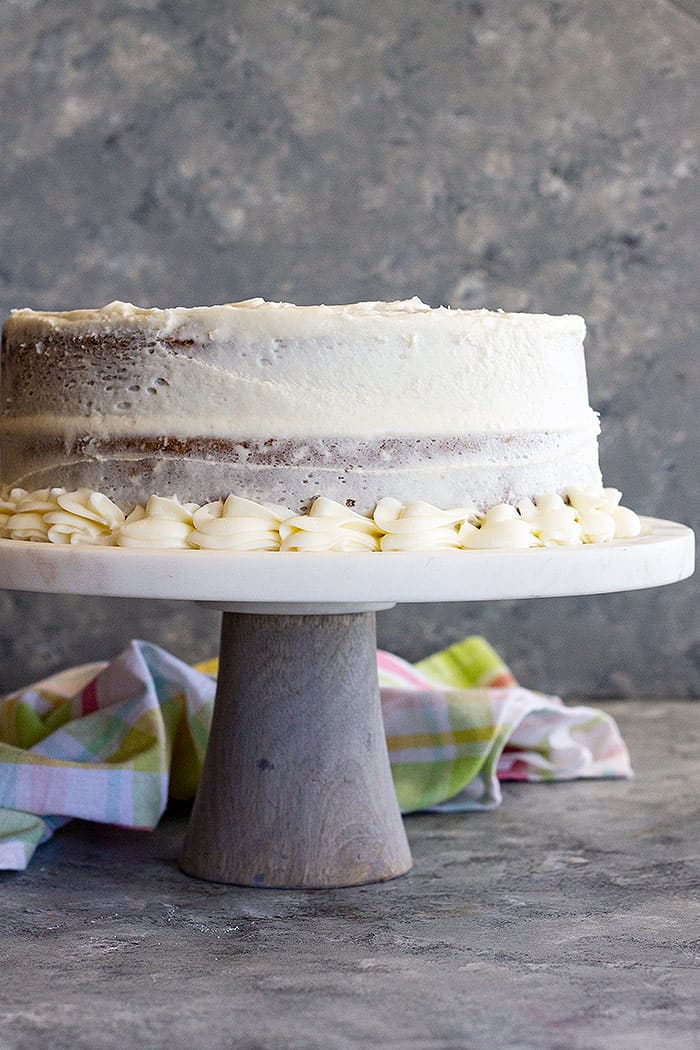 A cake on a stand covered in cream cheese frosting.