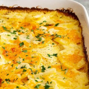 A large white dish with potatoes au gratin and garnished with parsley.