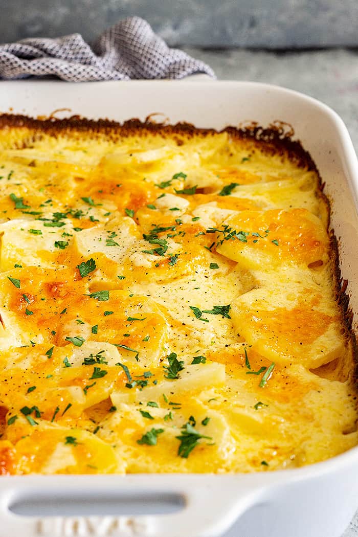 A large white dish with potatoes au gratin and garnished with parsley.