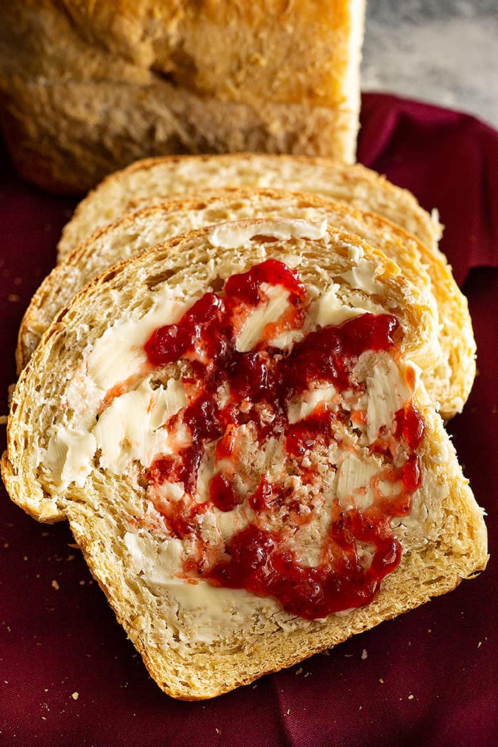 A slice of oatmeal sandwich bread smeared with butter and jam. 