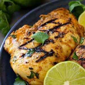 Grilled chicken on a blue plate garnished with lime and cilantro.
