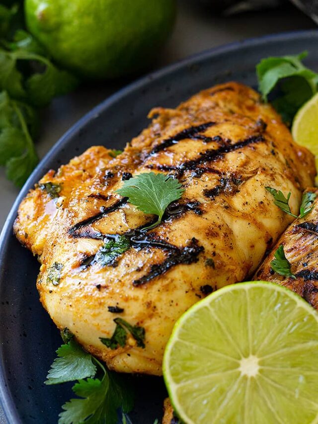 Grilled chicken on a blue plate garnished with lime and cilantro.