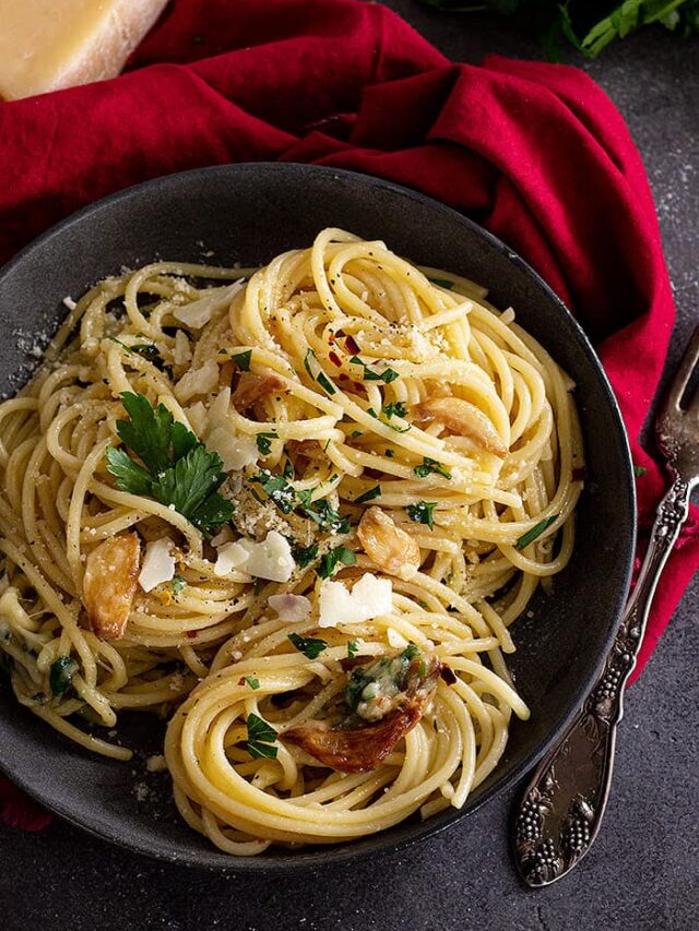 Top down view of spaghetti in a dark bowl and garnished with parmesan and parsley.