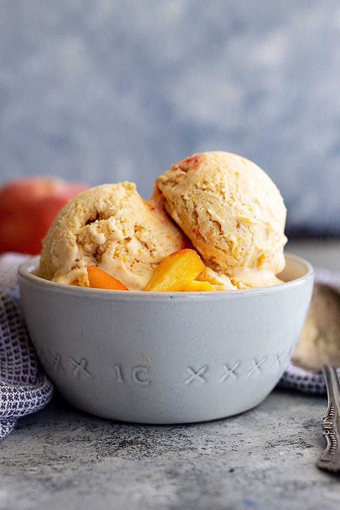 A bowl of peach ice cream topped with fresh peaches.