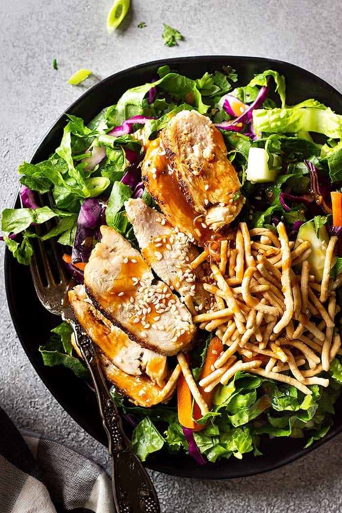 Top down view of salad drizzled with Asian dressing and sprinkled with sesame seeds and crunchy chow mein noodles.