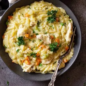 Top down image of orzo being served in a dark blue bowl and garnished with black pepper and parsley.