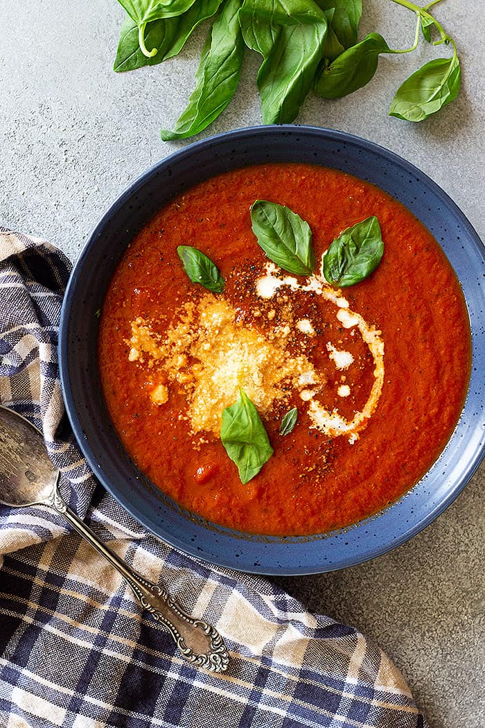 Top down view of a bowl of soup garnished with fresh basil, cream, cheese, and black pepper.