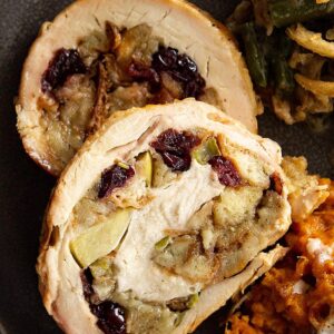 A close up view of the sliced turkey breast on a plate. You can see the stuffing with the apples and dried cranberries swirled in the turkey.