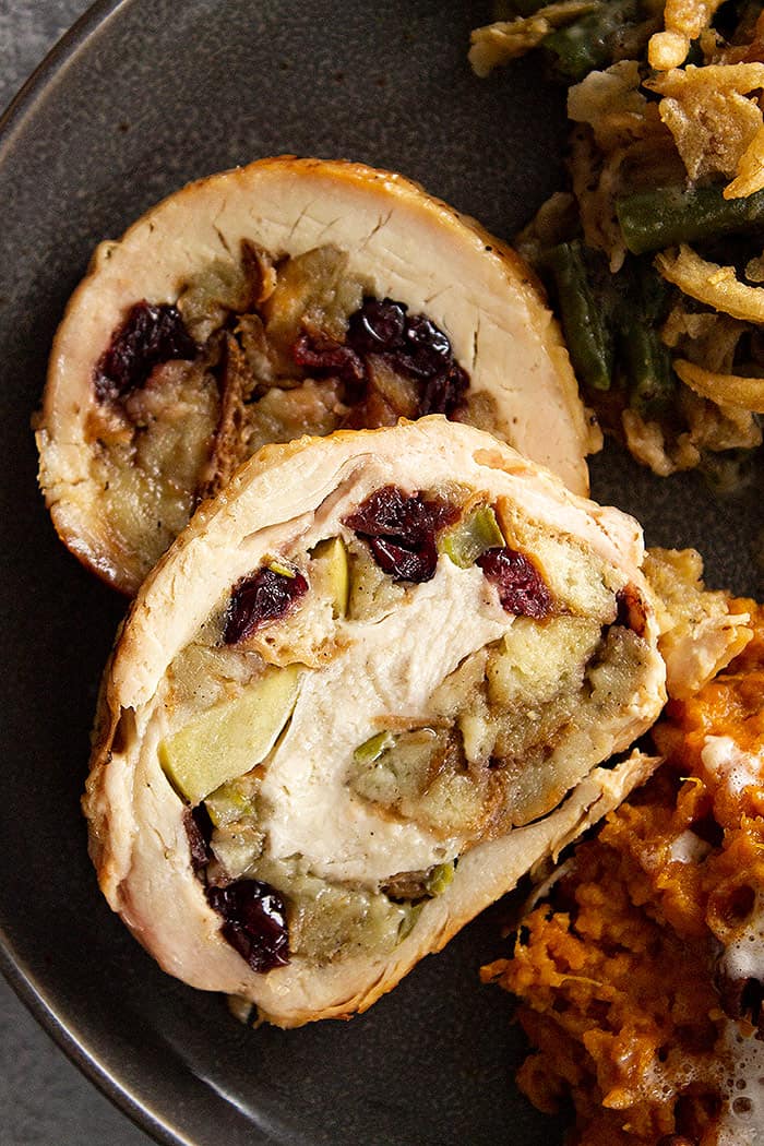 A close up view of the sliced turkey breast on a plate. You can see the stuffing with the apples and dried cranberries swirled in the turkey. 
