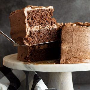 A large slice of chocolate cake with a smooth chocolate frosting is being lifted from the cake.