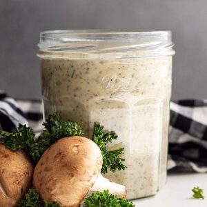 Cream of mushroom soup in a glass jar with fresh mushrooms and parsley as decoration to the side.