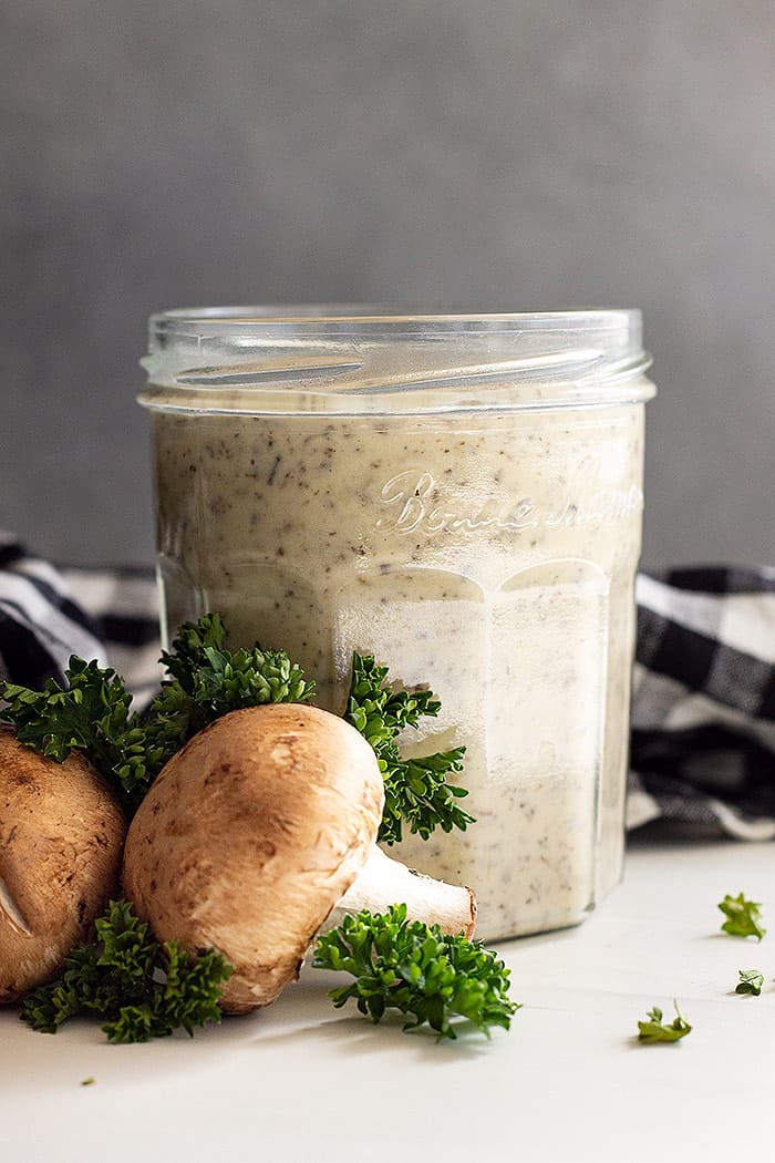Cream of mushroom soup in a glass jar with fresh mushrooms and parsley as decoration to the side. 