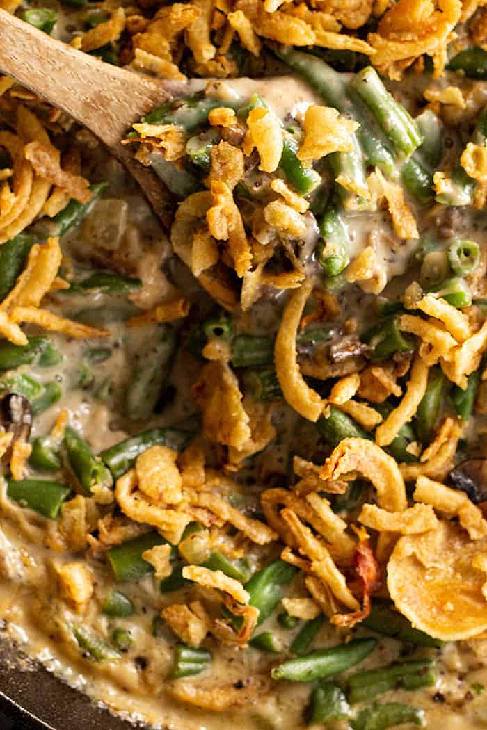 Wooden spoon stirring homemade green bean casserole with fried onion topping. 