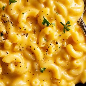 A close up of ultra creamy and cheese mac and cheese sprinkled with black pepper and a little parsley.