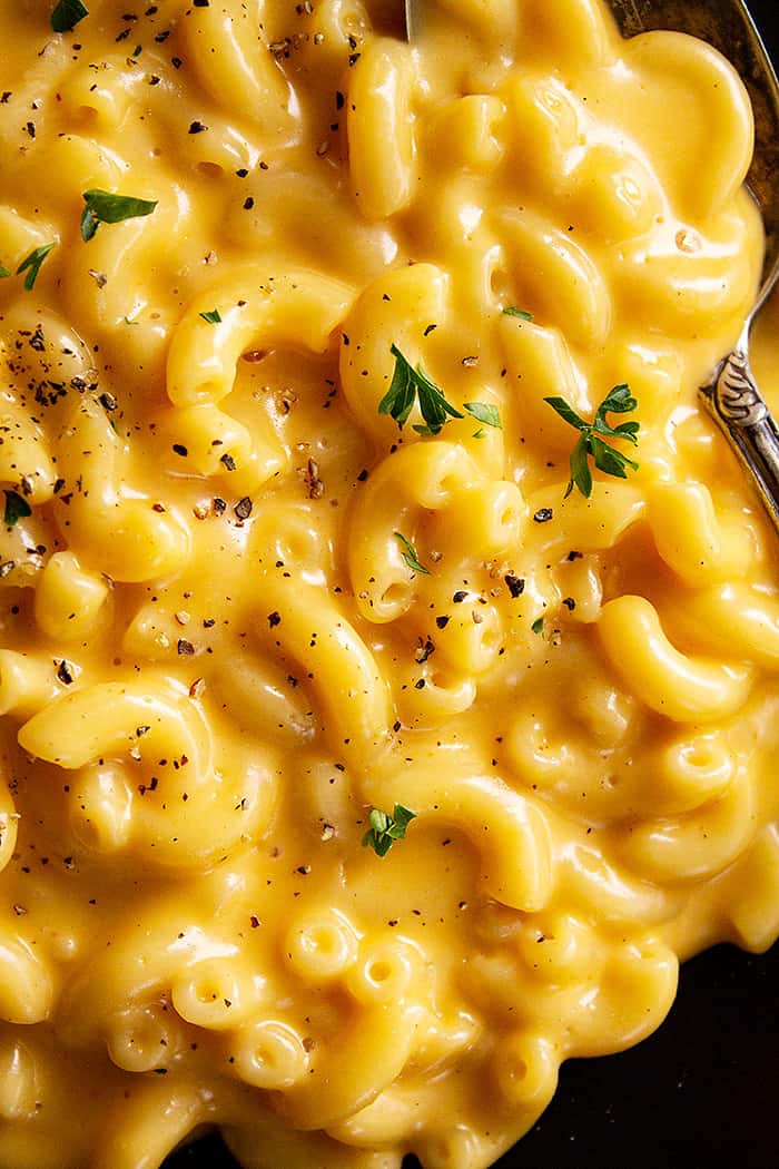 A close up of ultra creamy and cheese mac and cheese sprinkled with black pepper and a little parsley.