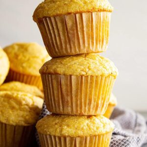 Three cornbread muffins stacked on top of each other with more muffins in the background.