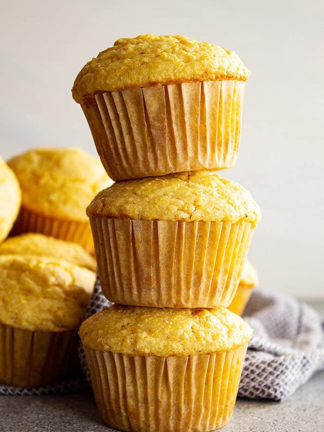 Three cornbread muffins stacked on top of each other with more muffins in the background.