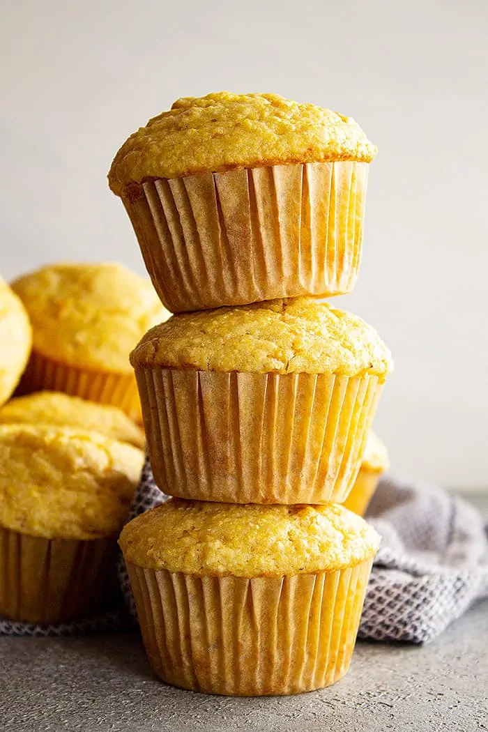 Three cornbread muffins stacked on top of each other with more muffins in the background. 