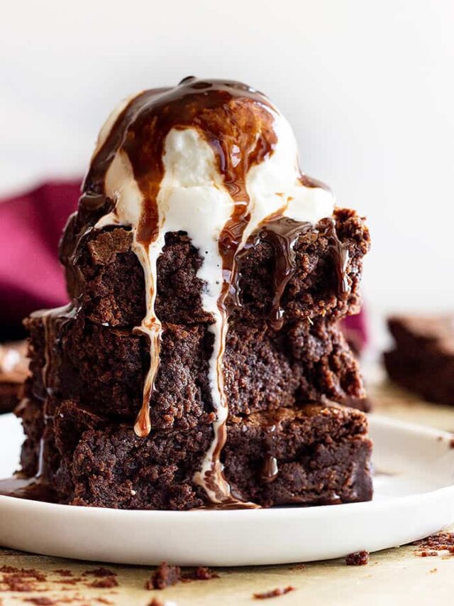 A stack of fudgy brownies topped with ice cream and hot fudge sauce.