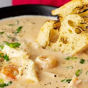 Close up of seafood bisque in a bowl with a piece of crusty bread dipping into it.