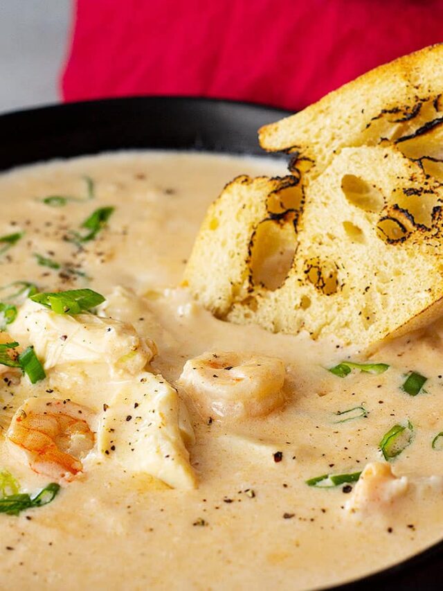 Close up of seafood bisque in a bowl with a piece of crusty bread dipping into it.